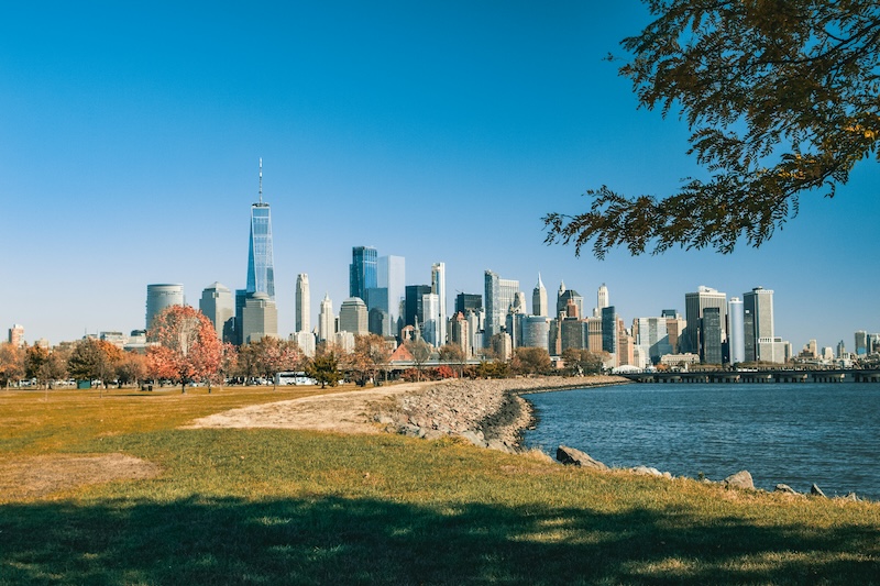 a photo of the jersey city skyline view from the very green and grassy liberty state park on a blue, sunny day