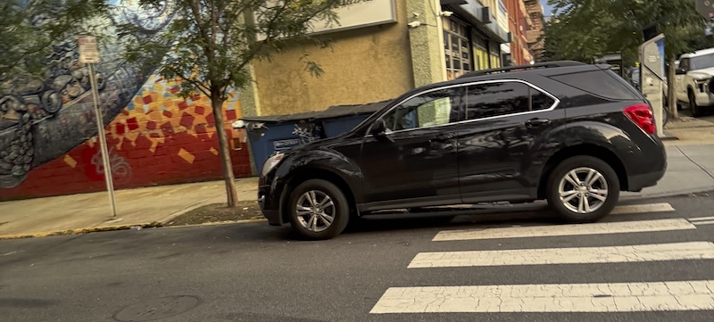 photo of a black suv parked on 80% of a crosswalk next to a grocery store