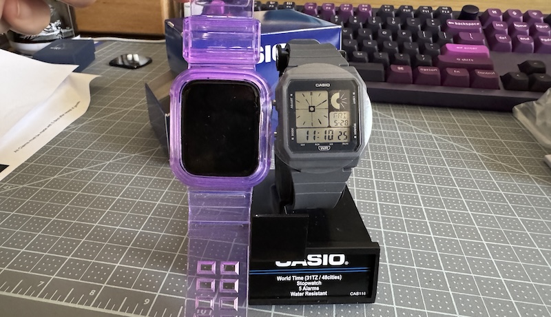photo of an apple watch with a clear/purple band held up next to a little-bit smaller gray casio watch before i removed the protective plastic