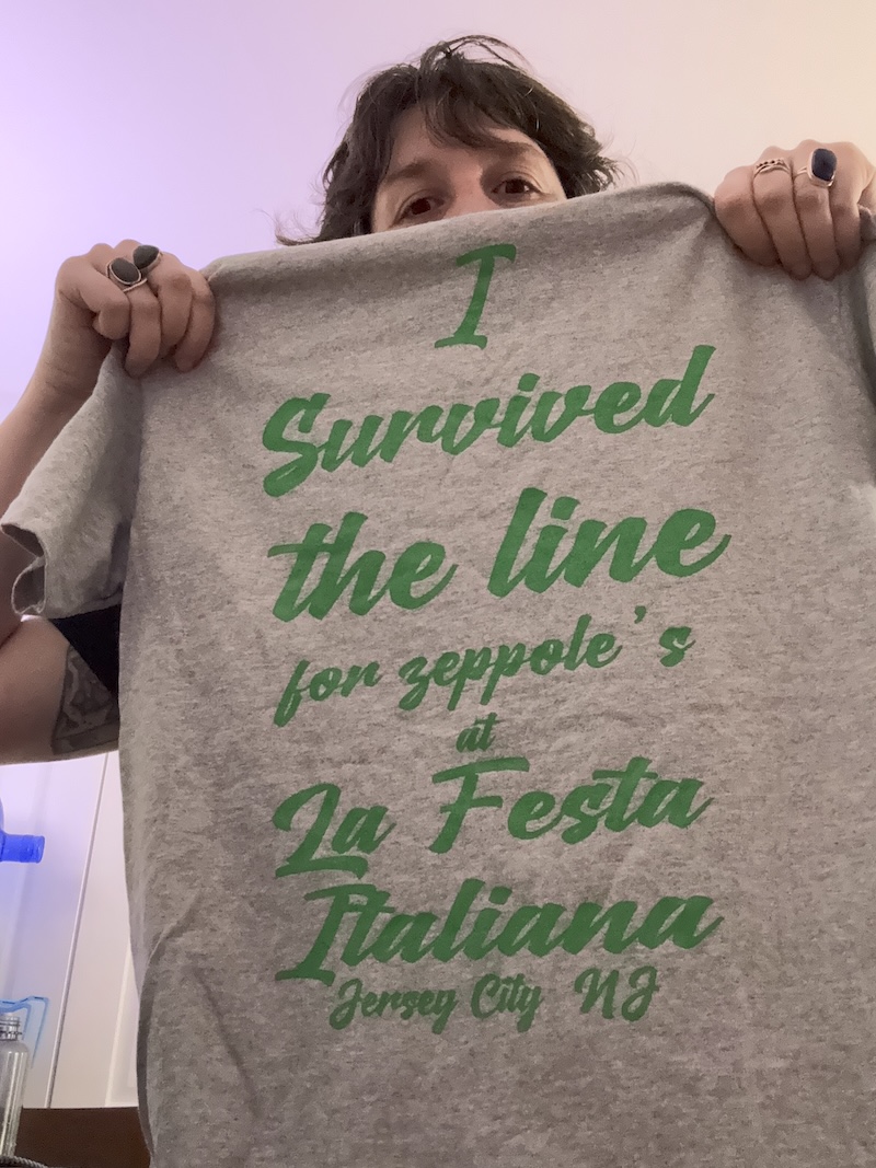 photo of me holding up a gray shirt with green text that says "i survived the line for zeppole's at la festa italiana jersey city nj"