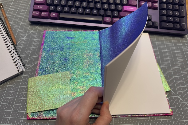 Photo of my hardcover book that I made opened up to show the iridescent bluish green endpaper