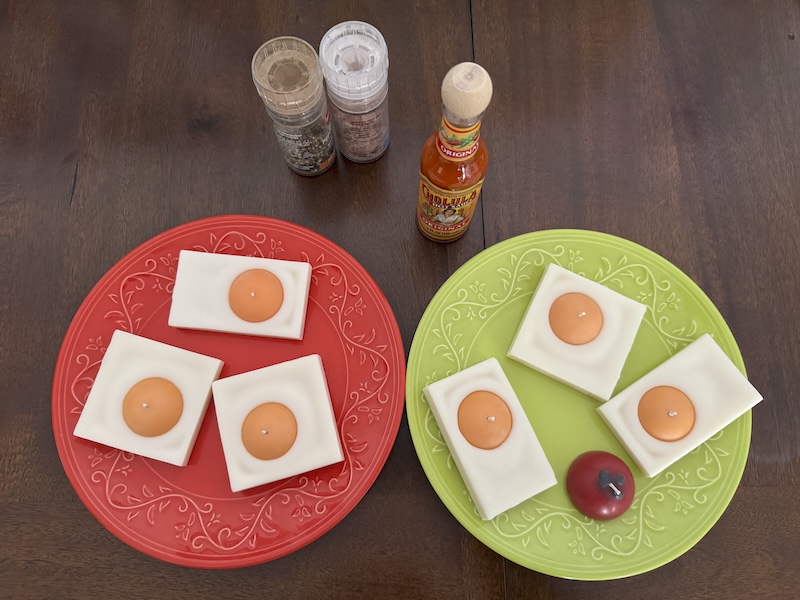 photo of my table that has two plates full of my pixel-art inspired egg tealight candles (and one little sample tomato candle) near salt and pepper grinders and a FRESH NEW bottle of cholula
