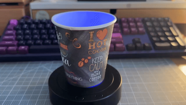 animated gif of a paper cup spining on a small usb-powered turn table. the cup says phrases about loving hot drinks like "i heart hot cocoa" "i dream in chocolate" "keep calm and make coffee"
