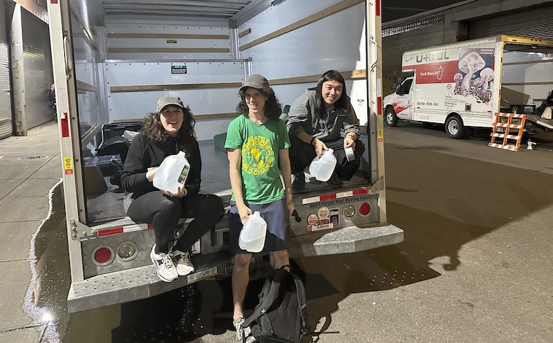 photo of me, jamie and yufeng holding water jugs sitting on the edge of the bed of our empty uhaul truck at 1am