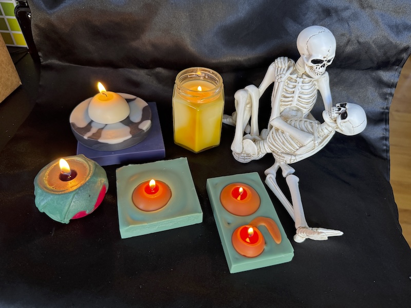 photo of my entire spooky candle collection surrounding a couple of skeletons in a sweet embrace, on a satin black pillowcase staged on my desk