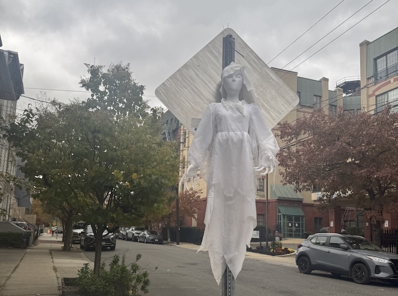 photo of a white spooky ghost lady halloween decoration hanging on the back of a street sign