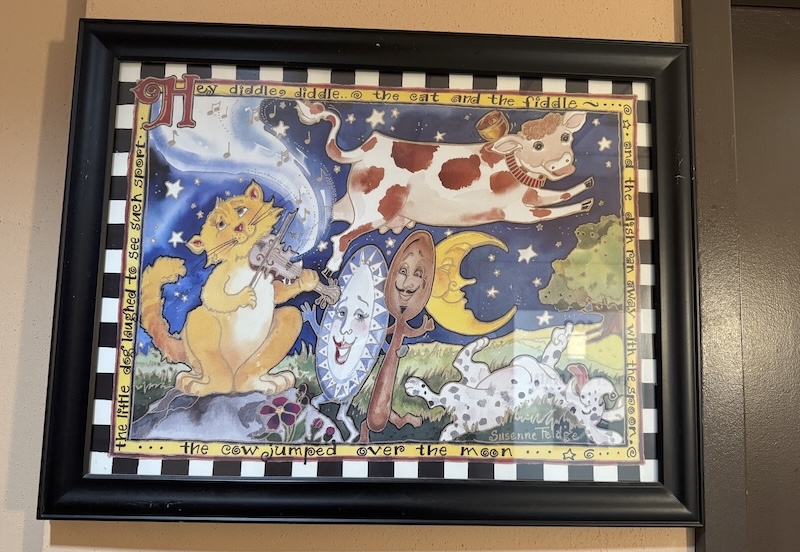 photo of an illustration of the "hey diddle diddle" poem that has a cat and a fiddle, plate and spoon, and a cow jumping over the moon