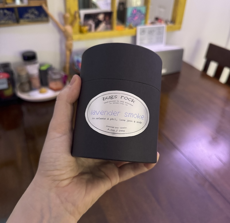 photo of me holding up a black cardboard tube container for my new candle called "lavender smoke" and on the label i wrote "to celeste and phil, love jenn and andy"