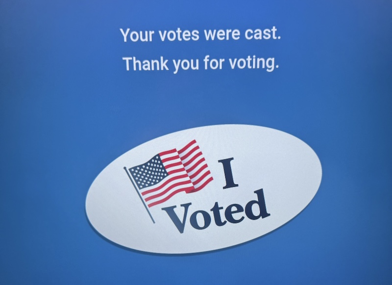 photo of voting booth screen that says "your votes were cast. thank you for voting." and then has an illustration of an oval "i voted" sticker with a waving american flag on it