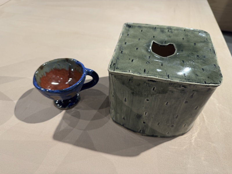 photo of a table with my two ceramic items: a small blue goblet and a gray tissue box cover with a cat head cut-out on top