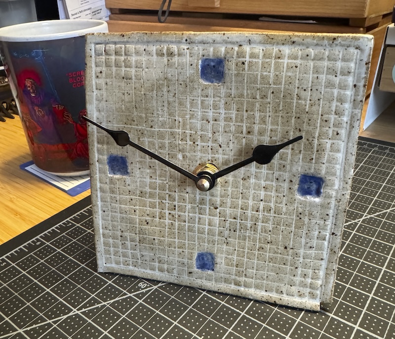 photo of a ceramic clock i made that's a flat square with a grid debossing, and i painted the pixels of the 3, 6, 9, and 12 hours