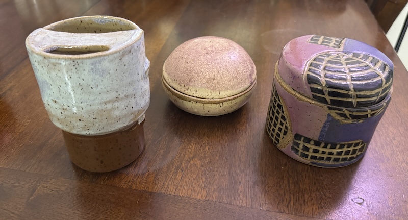 photo of a travel mug with light blue top and brown bottom, a closed vessel that's like a spherical clam-like orb in white and purple, and another closed vessel that's cylindrical and two different purples and carved black grid circles and rectangles