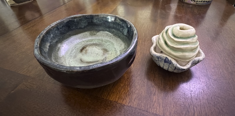 photo of a black clay hand-built matcha bowl with bluish green glaze inside, next to a porcelain cupcake bottom with cobalt wash and a swirly top with copper wash resting on top so it looks like a little treat