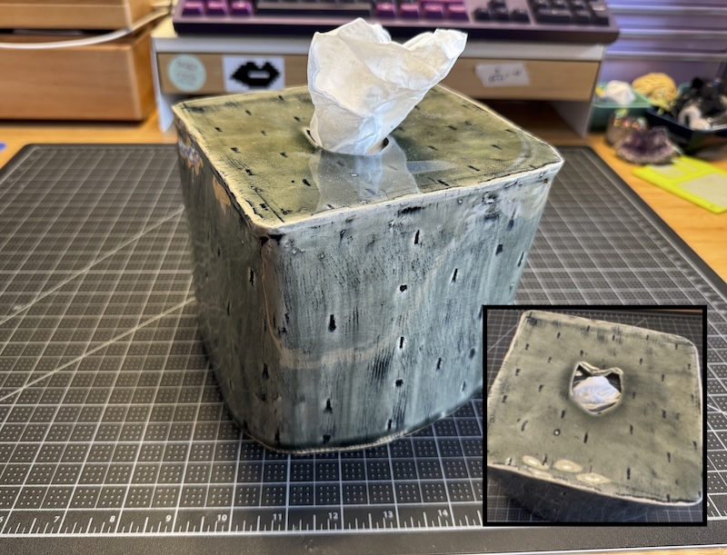 a ceramic tissue box cover with a cat head hole on top, with gray transparent glaze and tiny exclamation points stamped all over. i have a cut-out image on the corner to show the cat head hole without the tissue blocking it