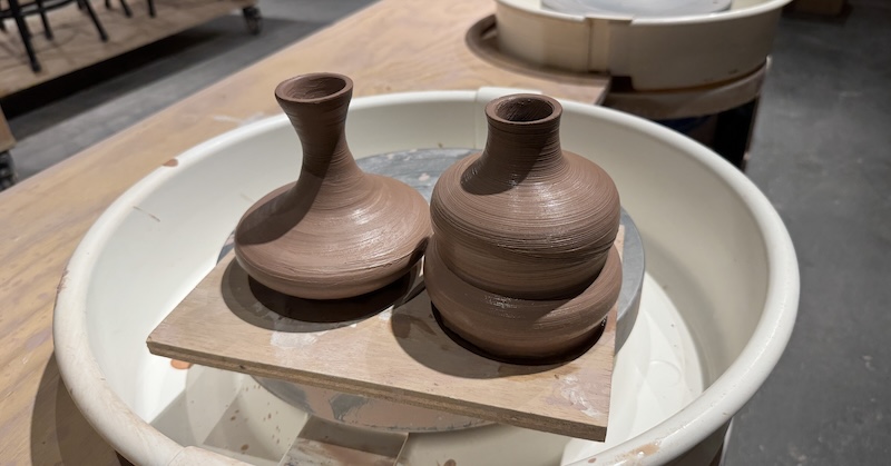 two freshly thrown potion bottle and vases that i made drying on a small board on a wheel