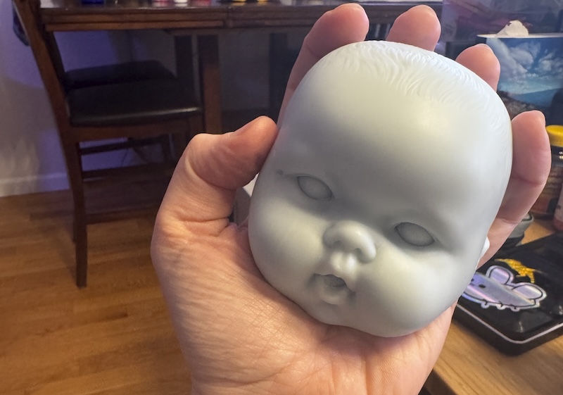 photo of my hand holding a bluish-gray wax mold of a doll head