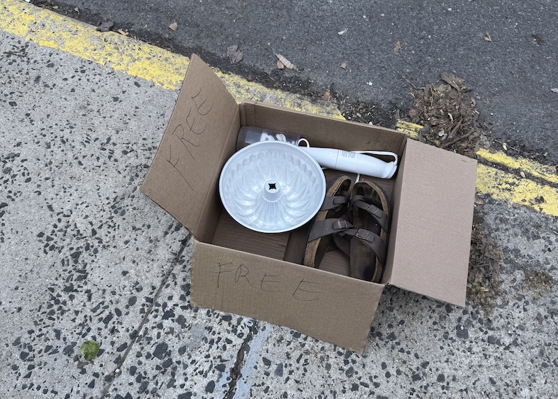 photo of a box marked "free" that has a bundt pan, leather sandals and what i think is an immersion blender inside on the street
