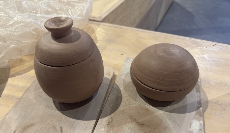 photo of two closed vessels i threw and trimmed at the ceramics studio. they look like urns, one has a handle i threw on it and the other is like a smooth orb