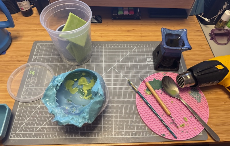 photo of my desk where i'm wax-painting inside a doll head mold and all my tools are around it
