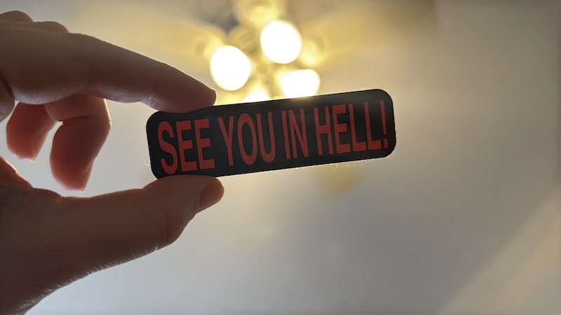 photo of my hand bringing into the frame a sticker that says "SEE YOU IN HELL"