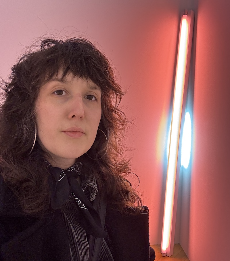 a selfie of me in front of a dan flavin installation inside mana contemporary, i'm drenched in pink and tangerine light from a flourescent stick bulb behind me