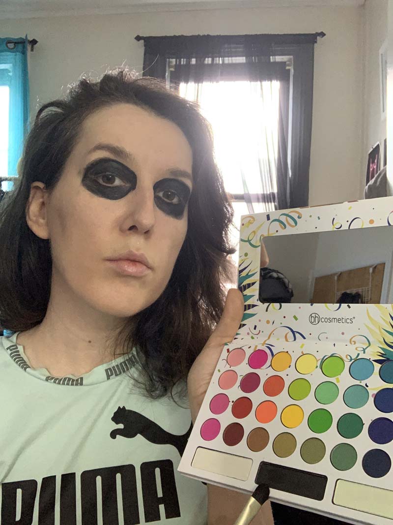 me holding up a rainbow eyeshadow palette and pointing the brush at the black pan