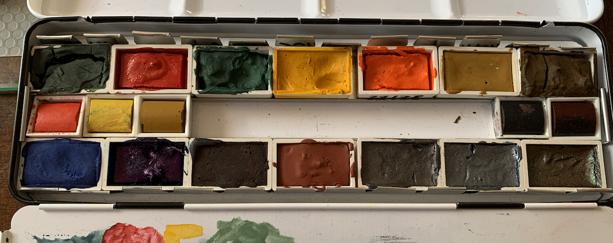 photo of a watercolor palette with a bunch of full pans of dried up or gooey watercolor paints