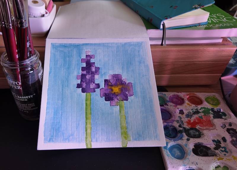 photo of pixel watercolor sketchbook on page 2, a couple of pixel art purple flowers