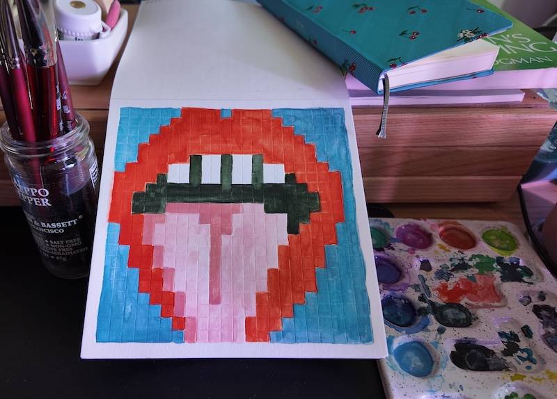 photo of pixel watercolor sketchbook on page 13, a pixel drawing of an open mouth with its tongue sticking out